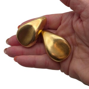 May include: Two teardrop-shaped objects with a smooth, metallic gold finish. Each piece features a rounded, bulbous base that tapers to a point, reflecting light across their polished surfaces. These solid, gold-colored items are presented together.