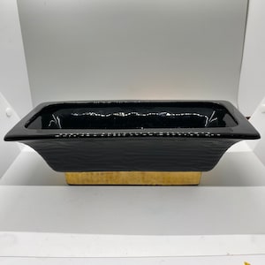 May include: A black ceramic planter with a gold rim. The planter has a rectangular shape and a slightly curved lip.