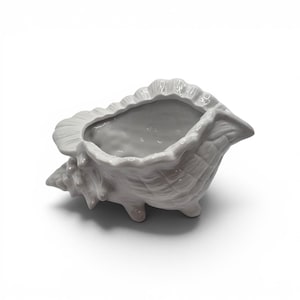 May include: A glossy, light gray ceramic bowl shaped like a conch shell. The vessel features a textured, ridged exterior with a wide, open top and a pointed end. It stands on small, integrated feet, showcasing a smooth, reflective finish throughout.