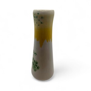 May include: A slender, ceramic vase with a cream-colored base and a yellow top that drips down. Green floral designs are painted on the vase. The vase is approximately 8 inches tall.