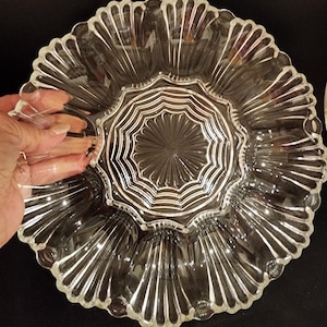 May include: A clear glass serving dish with a scalloped edge and a center section with a starburst pattern. The dish has six individual sections for serving appetizers or snacks.
