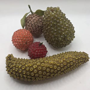 May include: A collection of decorative beaded fruit in various colors. Includes a brown sphere with green leaves, a green pear-shaped fruit, a red berry, an orange sphere, and a yellow, elongated fruit.
