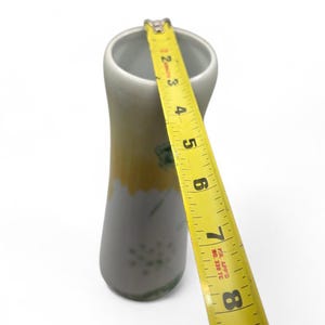 May include: A slender, cylindrical vase with a yellow and gray color scheme. The vase is approximately 8 inches tall, with a yellow band at the top and a gray base. A yellow measuring tape is placed next to the vase.