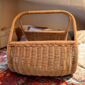 May include: Two woven wicker baskets, one inside the other. The larger basket has a curved handle and a rectangular shape. The smaller basket is rectangular and sits inside the larger one. Both are light brown.