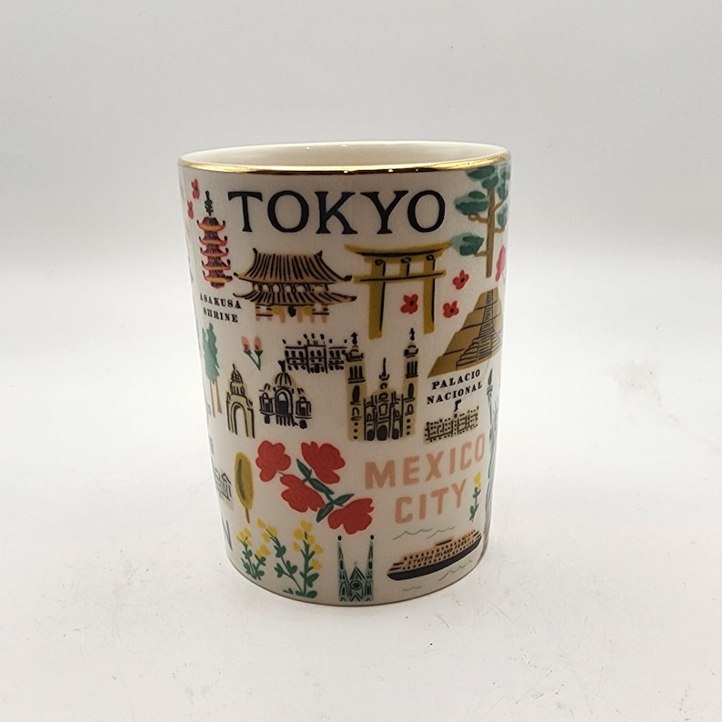 May include: A white ceramic travel mug with a gold rim, featuring colorful illustrations of landmarks and the city names "TOKYO" and "MEXICO CITY". The design includes pagodas, temples, and other architectural elements.