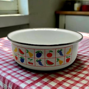May include: White enamel bowl with a silver rim, decorated with a colorful fruit pattern. The bowl sits on a red and white checkered tablecloth. The fruit illustrations include cherries, grapes, and watermelon.