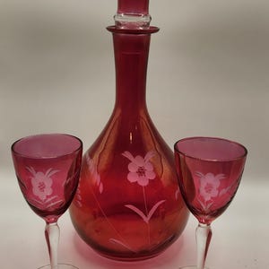 May include: A set of three ruby red glass decanter and two wine glasses with etched floral designs.