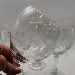 May include: Three clear wine glasses with etched floral designs and gold rims. The glasses have a classic, elegant shape, perfect for serving wine. The stemware is ideal for special occasions.