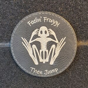 May include: A black leather patch with white stitching and the text "Feelin' Froggy Then Jump" and a white skeleton frog illustration.