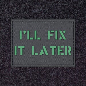 May include: A grey rectangular patch with the green text "I'LL FIX IT LATER". The patch has a dotted texture and a black border. The background is a dark, textured surface.