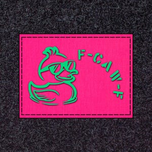 May include: A rectangular patch with a vibrant pink background and a green duck wearing sunglasses. The duck is outlined in green, and the text "F-CAW-F" is printed in green on the right side of the patch. The patch has a black border.
