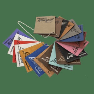 May include: A leatherette swatch book with a variety of colors and textures, including black, white, blue, red, brown, and teal. The swatches are labeled with the color and texture combination, such as "Black/Silver" and "Bamboo/Black".