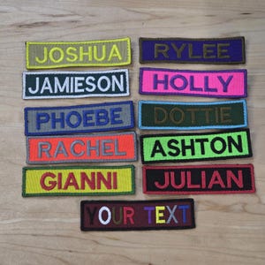May include: A selection of embroidered name patches in a variety of colours, such as yellow, purple, pink, and green. Each patch displays a different name in bold, contrasting thread. One patch reads "YOUR TEXT".