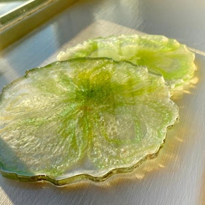 May include: Two green and white resin coasters with a swirled design. The coasters have a wavy edge and are made of clear resin with green and white swirls.