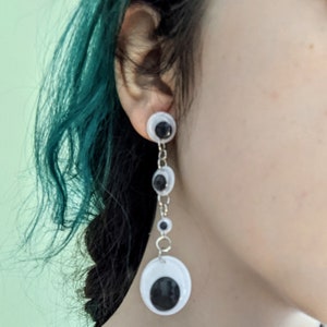 May include: A pair of dangling earrings with a silver chain and multiple white googly eyes. The eyes have black pupils.