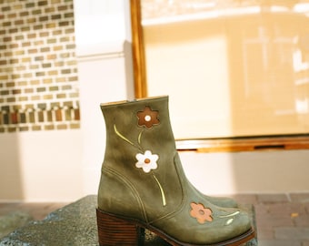 May include: Green ankle boots with a block heel and floral embroidery. The flowers are in shades of brown, white, and pink.