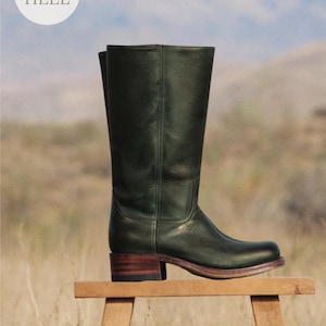 Könnte beinhalten: Ein wadenhoher Stiefel aus dunkelgrünem Leder mit niedrigem, geschichtetem Holzabsatz und abgerundeter Schuhspitze. Der Stiefel weist vertikale Nahtdetails entlang des Schafts auf. Eine kreisförmige weiße Grafik oben links enthält den Text LOW HEEL.