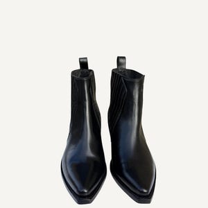 May include: A pair of black leather ankle boots with pointed toes. The boots have a pull tab at the top and elastic side panels. The boots are a classic style, suitable for various outfits.