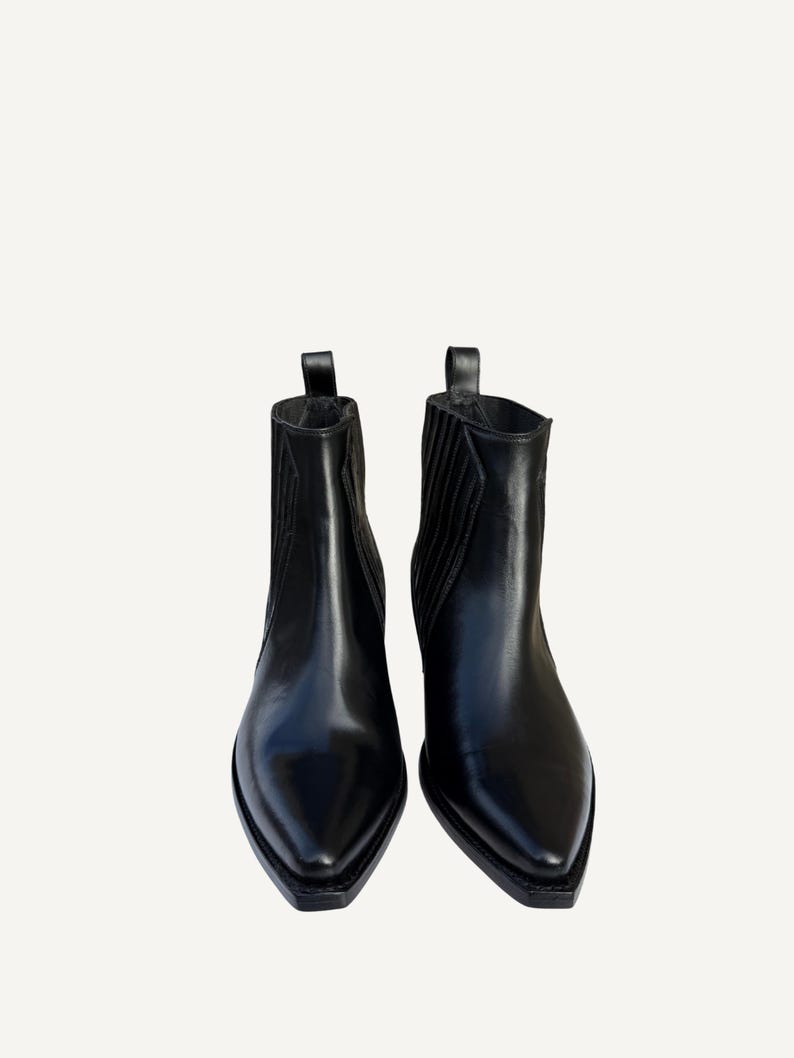 May include: A pair of black leather ankle boots with pointed toes. The boots have a pull tab at the top and elastic side panels. The boots are a classic style, suitable for various outfits.