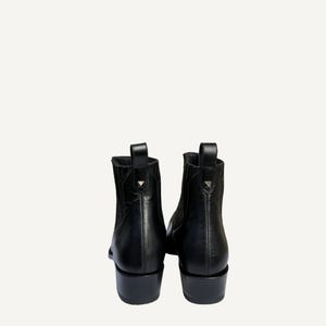 May include: A pair of black leather ankle boots. The boots have a pointed toe, a low block heel, and a pull tab at the back. A small silver stud is on the pull tab. The boots are shown from the back.