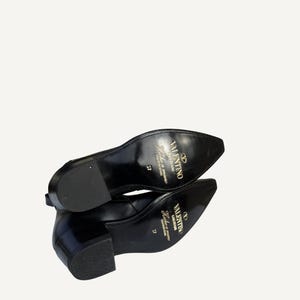 May include: Pair of black leather shoes with a pointed toe and a low block heel. The soles are visible, displaying the brand name "Valentino" in gold lettering. The shoes are size 37.