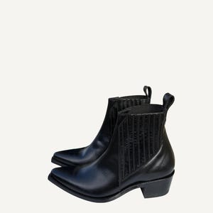 May include: A pair of black leather ankle boots with pointed toes and low heels. The boots have elastic side panels and pull tabs. The boots are a classic style, suitable for various outfits.