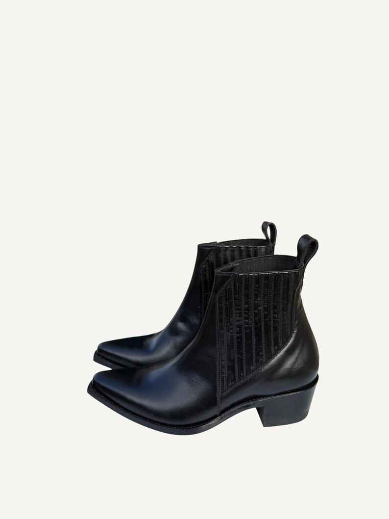 May include: A pair of black leather ankle boots with pointed toes and low heels. The boots have elastic side panels and pull tabs. The boots are a classic style, suitable for various outfits.