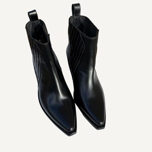 May include: A pair of black leather ankle boots with pointed toes. The boots have a pull tab at the back and a subtle, textured design on the sides. The boots are made of shiny, smooth leather.