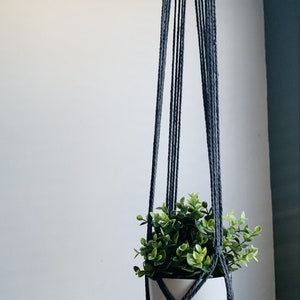 May include: A grey macrame plant hanger with a white pot and a green plant inside. The hanger is hanging from the ceiling.