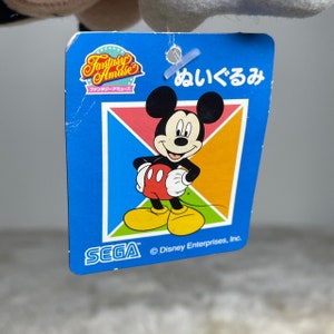 K&ouml;nnte beinhalten: Ein blaues Etikett mit wei&szlig;em Rand, das ein Cartoon-Bild von Mickey Mouse zeigt. Das Etikett tr&auml;gt die Aufschrift "Fantasy Amuse" und "SEGA" sowie den Text "&copy; Disney Enterprises, Inc." am unteren Rand. Das Etikett tr&auml;gt au&szlig;erdem den japanischen Text "めいくるみ", der mit "Make-up" &uuml;bersetzt werden kann.