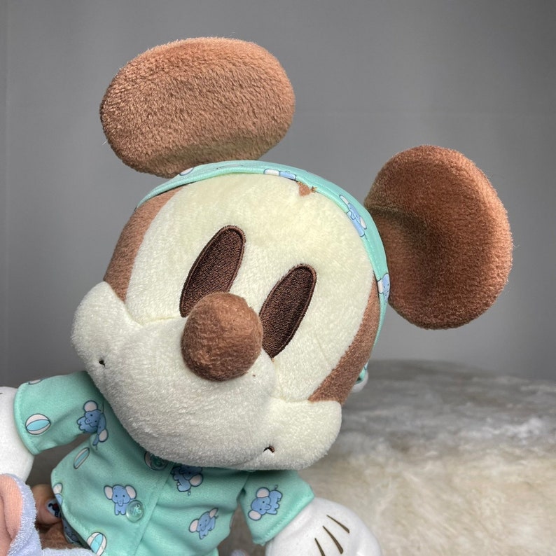 Może przedstawiać: Pluszowa zabawka Mickey Mouse w jasnoniebieskiej piżamie w białe wzory, z brązowymi uszami i brązowym nosem.