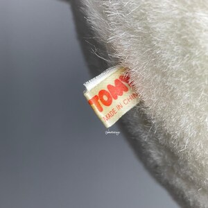 May include: A white plush toy with a yellow tag that reads "TOMMY MADE IN CHINA" in red lettering.