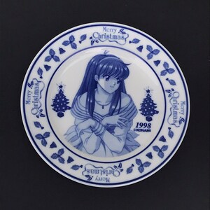 Op de afbeelding: Een blauw en wit keramiek bord met een kerstthema. Het heeft een vrouw met lang donker haar, een kerstboom en de tekst "Merry Christmas" en "1998 &copy;KONAMI".