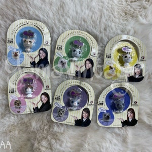 May include: Six colorful keychains featuring different cat breeds. Each keychain has a small plush cat charm and a metal ring. The keychains are packaged in plastic with a picture of the cat breed and the text "The Cat" in English and Japanese.