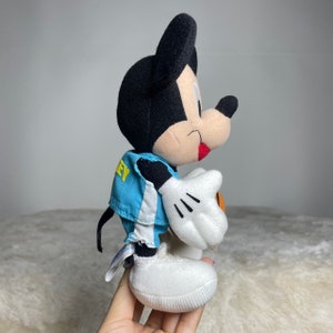 K&ouml;nnte beinhalten: Ein Pl&uuml;sch-Mickey-Mouse-Spielzeug, das eine blaue und wei&szlig;e Basketballuniform tr&auml;gt und einen Basketball h&auml;lt. Das Spielzeug hat eine schwarze Nase und rote Wangen.