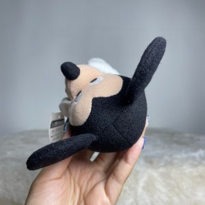 K&ouml;nnte beinhalten: Ein schwarzes und wei&szlig;es Pl&uuml;schtier von Mickey Mouse mit einem erhobenen Ohr. Das Spielzeug ist aus weichem, flauschigem Stoff und hat ein aufgen&auml;htes L&auml;cheln.