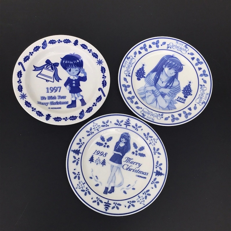 Op de afbeelding: Drie blauwe en witte keramische borden met een kerstthema. Elk bord heeft een ander anime-personage en het jaar 1997, 1998 of 1998. De borden hebben een blauwe en witte hulstborder.