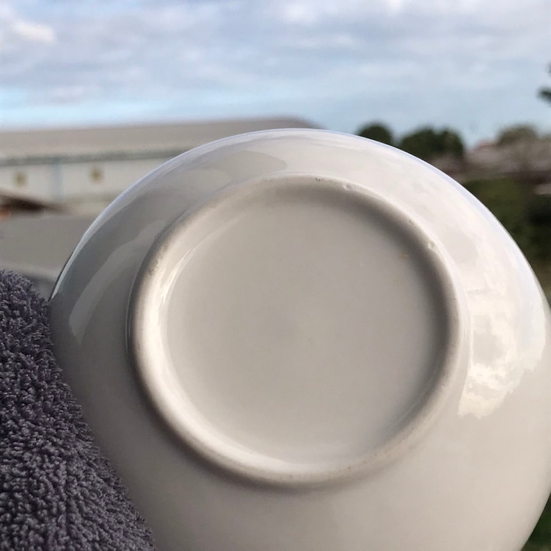 May include: The underside of a white ceramic saucer. The saucer is smooth and has a slightly raised edge.