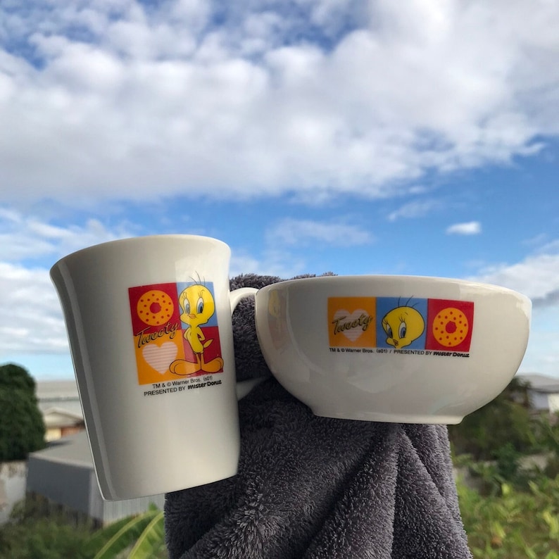 May include: A white ceramic mug and bowl with a Tweety Bird design. The mug and bowl feature a yellow Tweety Bird with a red heart and a donut. The text "Tweety" is printed on both pieces. The text "TM & &copy; Warner Bros. 1997" and "Presented by Mister Donut" is printed on the bowl.