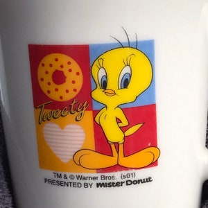 May include: A white ceramic mug with a colorful cartoon image of Tweety Bird. The image includes a donut, a heart, and the text "Tweety". The mug is a promotional item from Mister Donut.