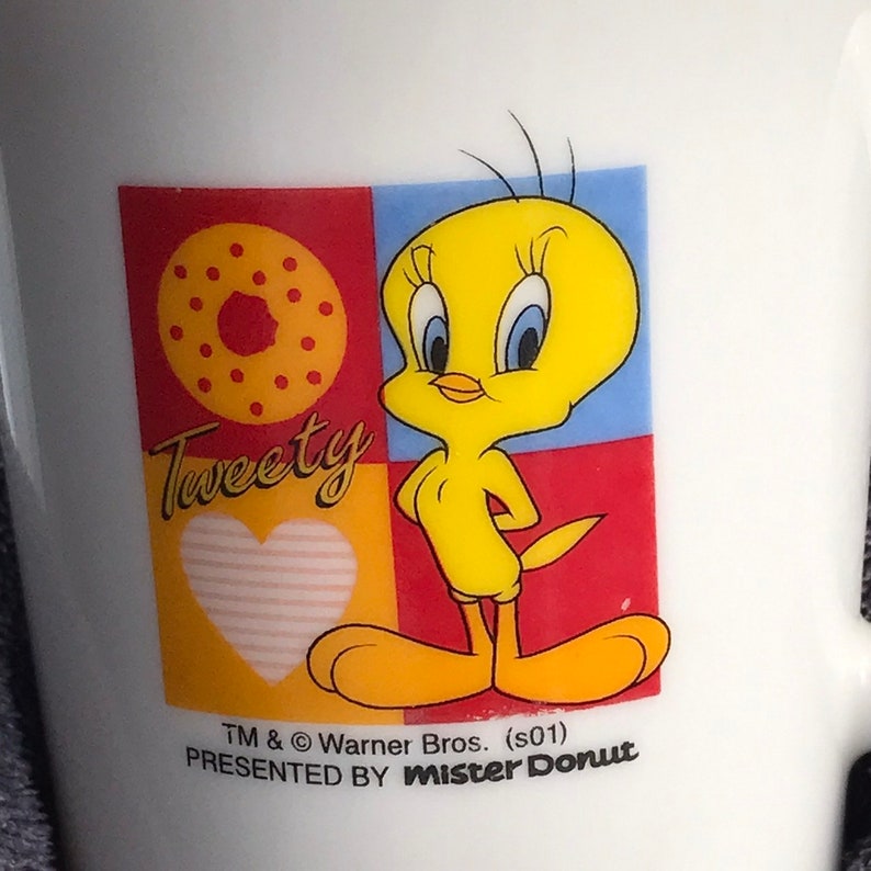 May include: A white ceramic mug with a colorful cartoon image of Tweety Bird. The image includes a donut, a heart, and the text "Tweety". The mug is a promotional item from Mister Donut.