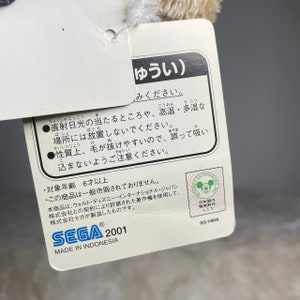 May include: A white plush toy with a tag that reads "ゆうい) みください." The tag also includes instructions for care, such as avoiding direct sunlight and high temperatures, and a warning about the toy's tendency to shed. The tag also states that the toy is made in Indonesia and is for ages 6 and up.