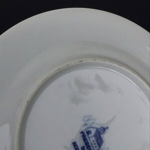 Op de afbeelding: De onderkant van een wit keramiek bord met een blauw en wit logo met de tekst "Gedrukt door  Gemaakt in  Engeland".