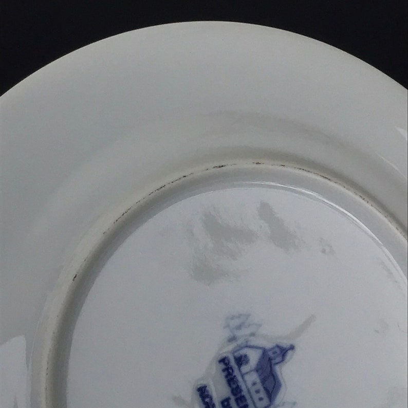 Op de afbeelding: De onderkant van een wit keramiek bord met een blauw en wit logo met de tekst "Gedrukt door  Gemaakt in  Engeland".