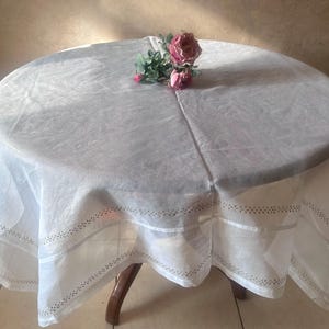 May include: White tablecloth with a delicate lace trim and a small bouquet of pink roses in the center.