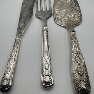 Può includere: Un set di tre posate argentate con manici decorati. Il set comprende un coltello, una forchetta e un coltello per torta.