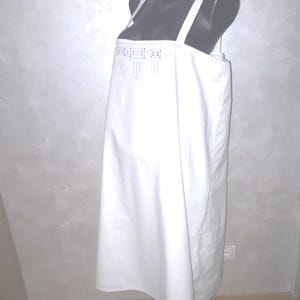 Puede incluir: Un vestido blanco sin mangas con un diseño geométrico en el escote. El vestido está en un maniquí y tiene una silueta simple y fluida.
