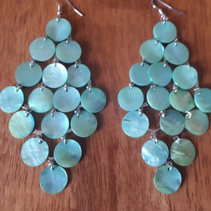 以下が含まれることがあります： カスケードデザインのドロップイヤリングのペア。イヤリングはシルバーメタル製で、複数の丸いライトブルーの虹色の貝殻のようなパーツが特徴です。