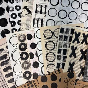 May include: A collection of handmade paper ephemera with black ink designs. The designs include circles, musical notes, and abstract shapes. Some papers have text from vintage books. The words "Notice how much" are visible on one sheet.