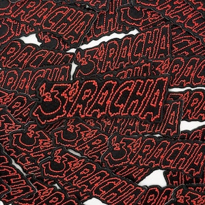 Puede incluir: Un conjunto de parches bordados negros con la palabra "SRACHA" en rojo. Los parches están dispersos sobre una superficie blanca, mostrando las letras audaces y estilizadas.